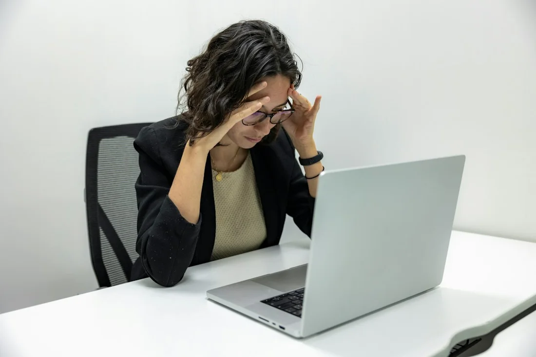A person sits at a laptop with their head in their hands, overwhelmed.